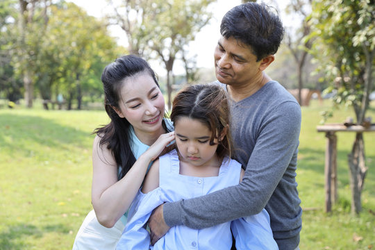 image of happy family, father and mother are comforting their depressed daughter with a smiling and warm face during holiday vacation in the park