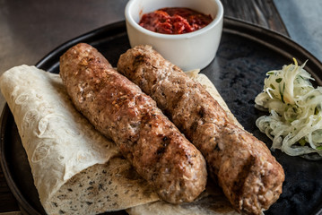 Two lula kebabs on pita bread with onions and red tomato sauce