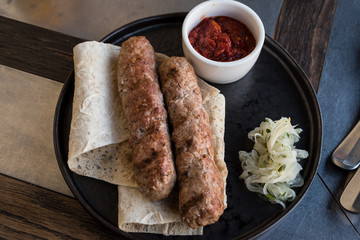 Two lula kebabs on pita bread with onions and red tomato sauce