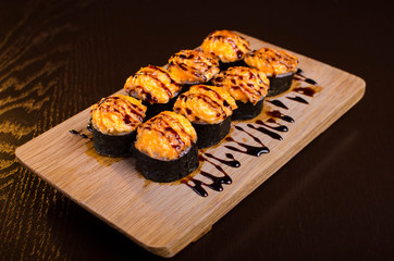 Japanese maki rolls baked with cheese and sprinkled with sauce. Sushi on a wooden plank. Seafood menu on black background