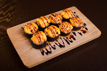 Japanese maki rolls baked with cheese and sprinkled with sauce. Sushi on a wooden plank. Seafood menu on black background
