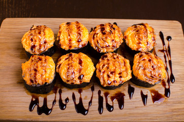 Japanese maki rolls baked with cheese and sprinkled with sauce. Sushi on a wooden plank. Seafood menu on black background