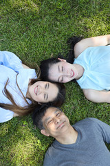 top view of lovely and joyful family looking at camera and smiling while lying on the grass filed during summer time