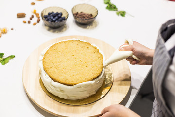 Confectioner with pastry bag squeezing cream on cake at kitchen. The concept of homemade pastry, cooking cakes.