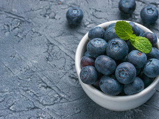 Freshly picked blueberries closeup. Ripe and juicy fresh blueberry with green mint leaves on textured concrete background. Bilberry on gray background with copyspace. Top view or flat lay