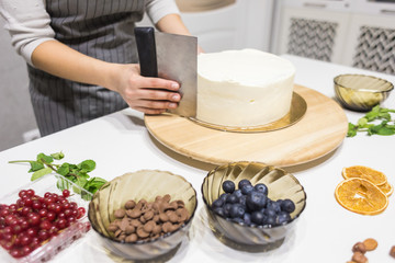 Obraz na płótnie Canvas Confectioner smooths white cream on a biscuit cake with a cooking spatula. The concept of homemade pastry, cooking cakes.