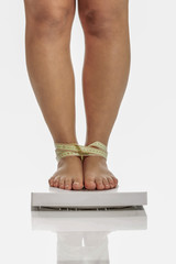 Oversize woman legs standing on weight with measure tape wrapped on ankles.