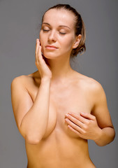 Young nude woman with covered breast touching face. Skin pampering concept.
