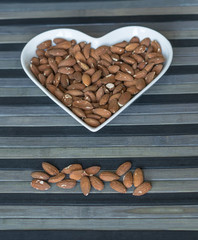 Nuts arranged in heart  on background. Healthy Food image close up almond on the cup plate. Love Texture on top view mock up