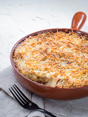 Close up view of appetizing potato casserole with fish, eggs and cream. Potato casserole in serving baking pan on white concrete background