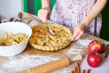 woman adds sliced apples to apple pie. Woman hands working a pie dough in a tray, on a kitchen table, surrounded by pumpkin pie ingredients. Traditional pies baking