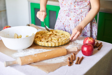 Obraz na płótnie Canvas woman adds sliced apples to apple pie. Woman hands working a pie dough in a tray, on a kitchen table, surrounded by pumpkin pie ingredients. Traditional pies baking