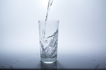 Pour clean drinking water into the glass on the table. Close-up.