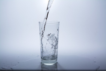 Pour clean drinking water into the glass on the table. Close-up.