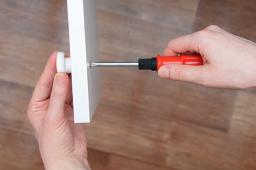 Furniture assembly. Hands of the girl close up. A screwdriver fastens the white knob to the cabinet door.