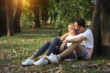 young couple people are in love, sitting and embracing in park during summer season with trees (friendship or valentine concept)