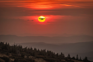 Sunset in the mountains with plane in the sun