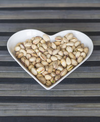 Nuts arranged in heart  on background. Healthy Food image close up pistachios on the cup plate. Love Texture on top view mock up