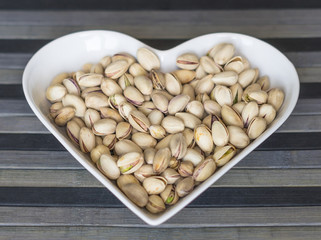 Nuts arranged in heart  on background. Healthy Food image close up pistachios on the cup plate. Love Texture on top view mock up
