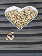 Nuts arranged in heart  on background. Healthy Food image close up pistachios on the cup plate. Love Texture on top view mock up