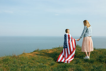 single mother with son on independence day of USA. Woman and her child walk with the USA flag on the ocean coast