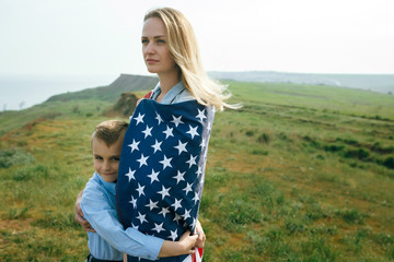 single mother with son on independence day of USA. Woman and her child walk with the USA flag on...