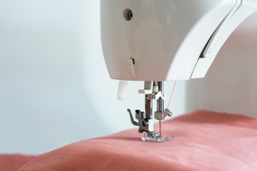 Close up of foot of sewing machine of white sewing machine while working on process with pink linen fabric on white background.