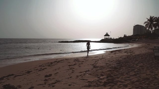 Woman walking along the golden beach at sunset. Shot in Jamaica, Caribbean 