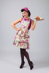 Beautiful young housewife in purple dress and apron with dessert.