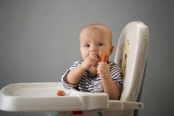 Funny baby 10 months eating sausages in highchair
