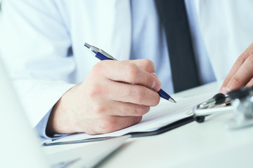 Mid section of male doctor writing write prescription to patient at worktable. Panacea and life save, prescribing treatment.