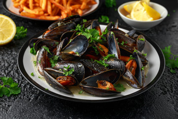Mussels with white wine, garlic, lemon and herbs in a plate, French fries. rustick background. Seafood.