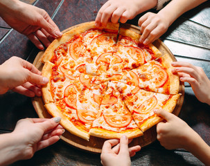 Hands taking pizza slices from wooden table, close up view.