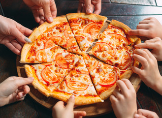 Hands taking pizza slices from wooden table, close up view.