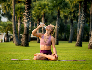 Beautiful young woman practic yoga at the beach. Early morning exercise. Drinking water. Sunrise