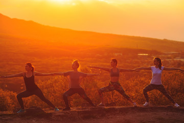 Silhouette of young womans practicing yoga or pilates at sunset or sunrise in beautiful mountain location.