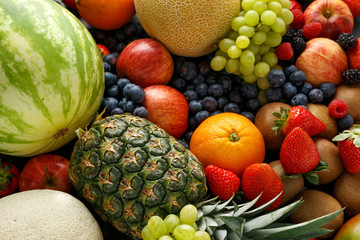 Variety of fresh fruits and berries on dark background: cantaloupe, melon, watermelon, blueberry, oranges, apple, strawberry, pineapple, mango, grapes and kiwi.