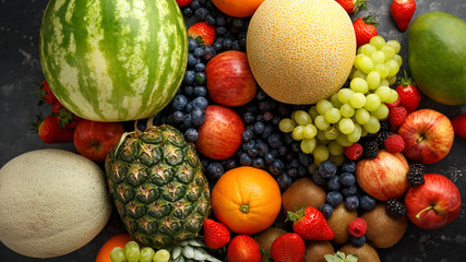 Variety of fresh fruits and berries on dark background: cantaloupe, melon, watermelon, blueberry, oranges, apple, strawberry, pineapple, mango, grapes and kiwi.