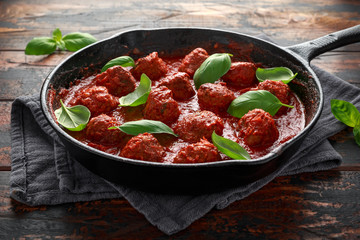 Homemade Meatballs in iron cast with sweet and hot tomato sauce, basil. On wooden table