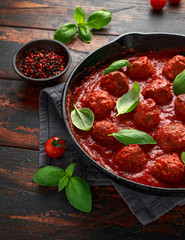 Homemade Meatballs in iron cast with sweet and hot tomato sauce, basil. On wooden table