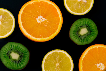 Colorful fresh fruits on a dark background. Orange, mandarin, kiwi, lemon. Fruit background. Summer food concept.