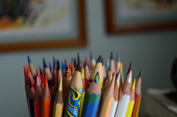 Fototapeta premium many colored pencils in the stand on the background of paintings