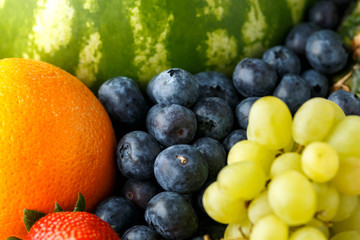 Variety of fresh fruits and berries on dark background: cantaloupe, melon, watermelon, blueberry, oranges, apple, strawberry, pineapple, mango, grapes and kiwi.