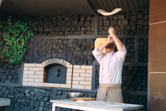 Skilled chef preparing dough for pizza rolling with hands and throwing up.