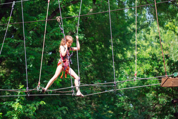 Happy school girl enjoying activity in a climbing adventure park on a summer day,