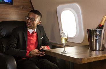 Successful young Afro American black businessman sitting in the chair of his private jet