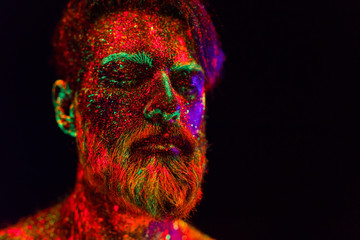 Concept. Portrait of a bearded man. The man is painted in ultraviolet powder.