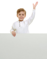 A little boy is looking from behind an empty banner.