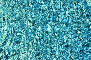 Texture of crumpled foil with a holographic blue-green glow