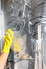 Close-up of a woman in uniform and yellow gloves washes a windows with window scraper. Professional...